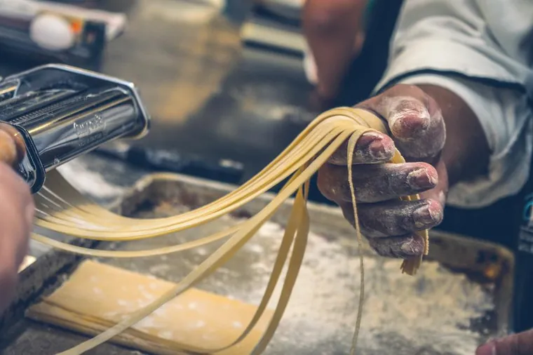 A cook's hands pulling fresh pasta in a working kitchen