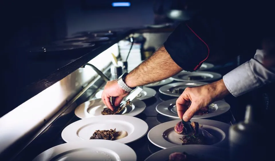 A chef's hands plating dishes at the pass during service