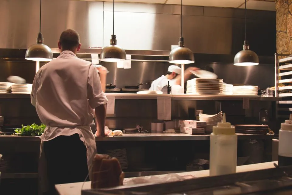 Cooks working the line in an open restaurant kitchen under warm pendant lights