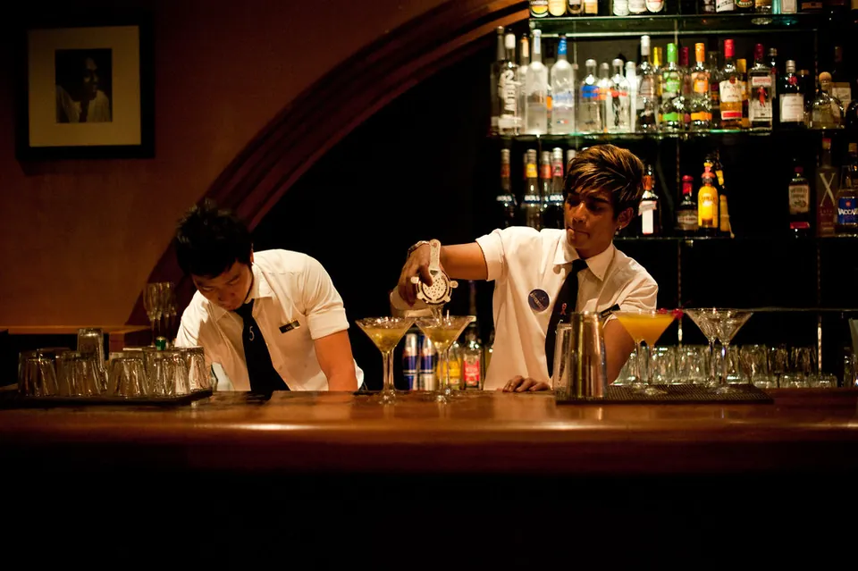 Bartenders mixing drinks behind a warm wood bar